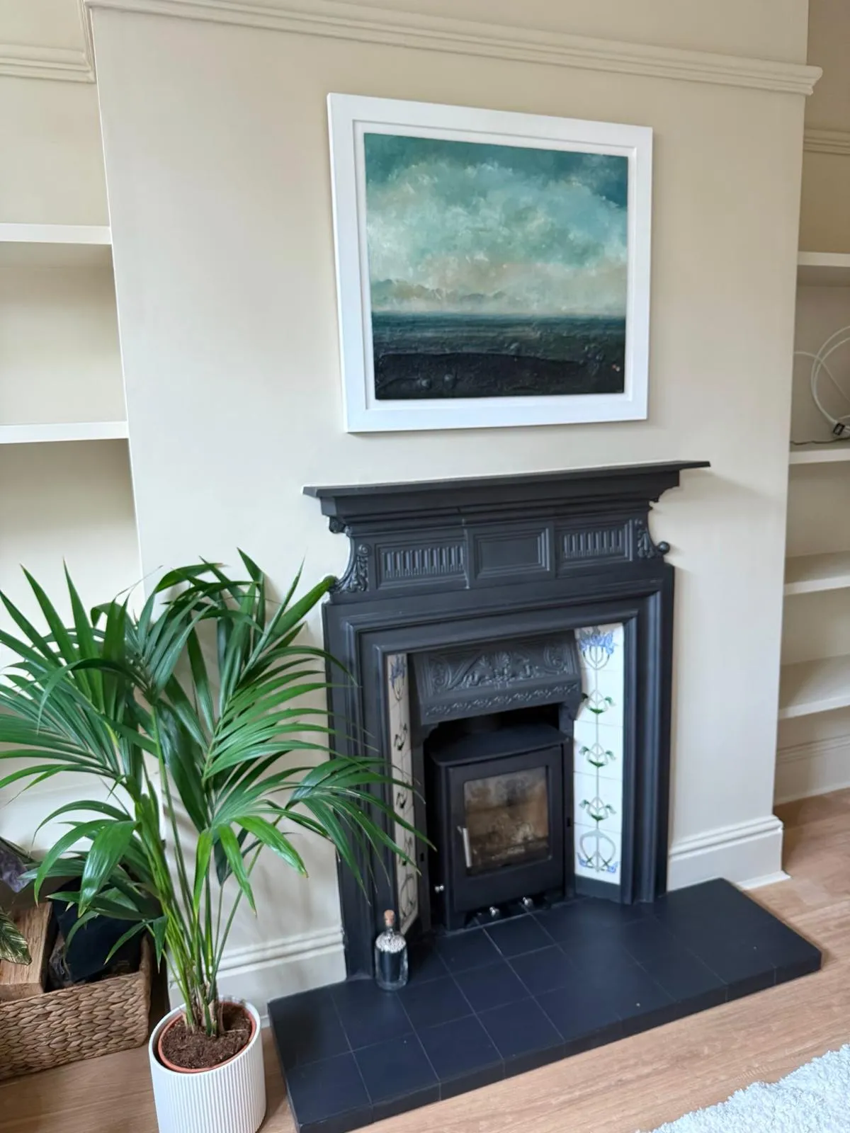 Cast-iron fireplace and inset stove in an alcove beneath a seascape painting
