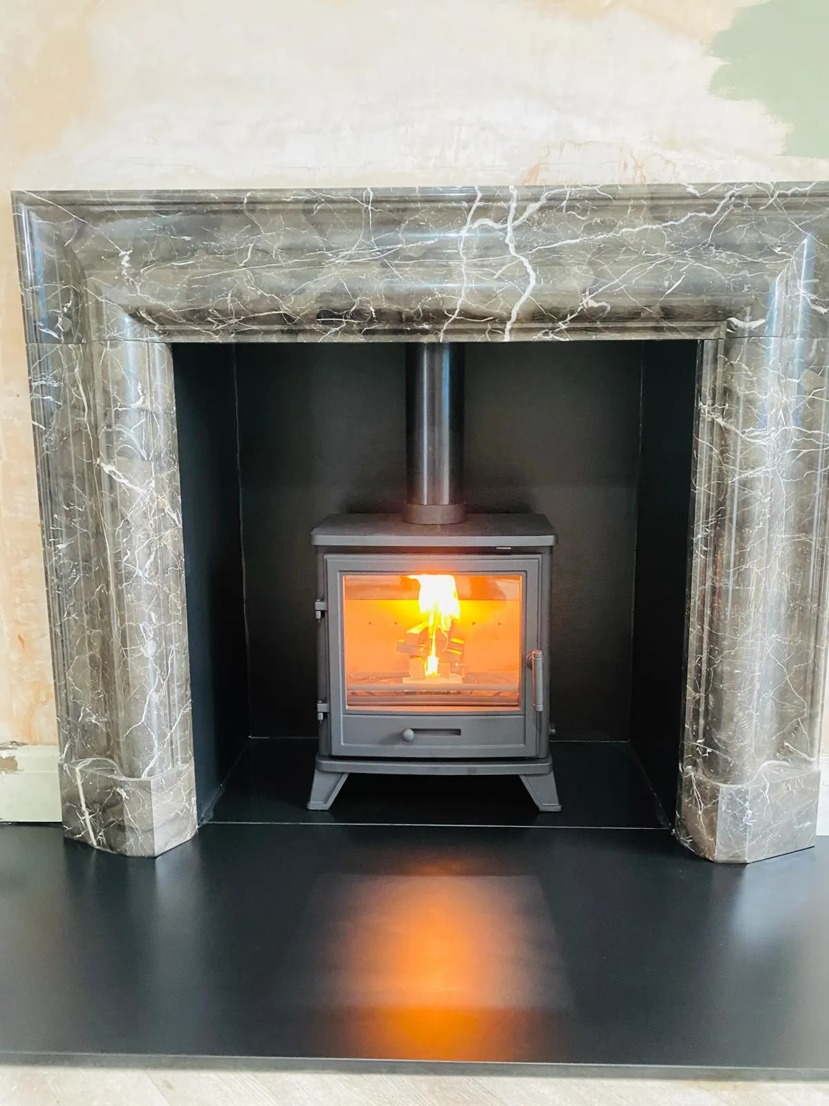Stove lit inside a grey marble bolection fireplace with a black-lined chamber and hearth